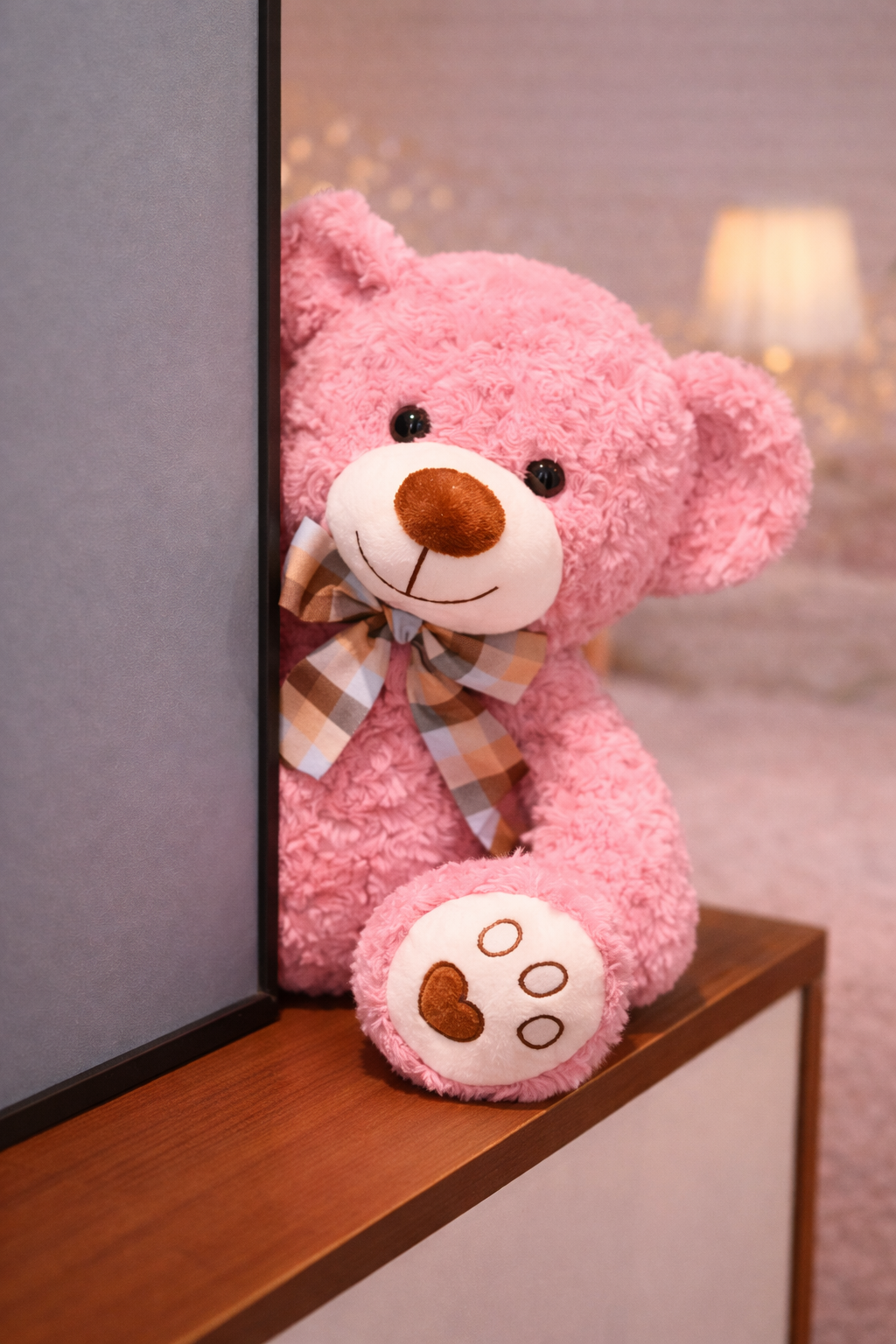 Pink teddy bear with a bow on a wooden shelf against a blurred background